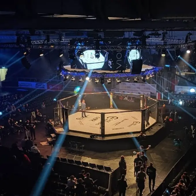 Arena MMA event with custom branded cage canvas under fight-night spotlights